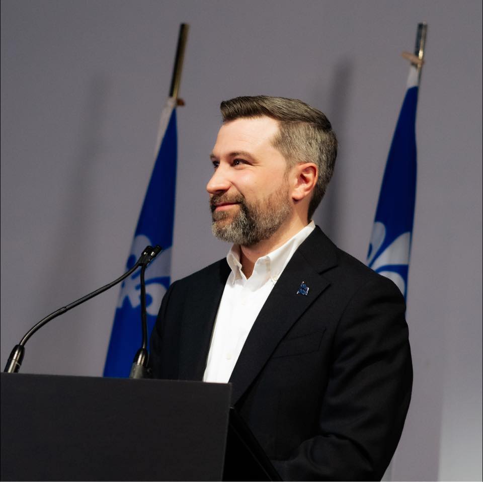 Gabriel Nadeau-Dubois à un lutrin, devant des drapeaux du Québec.